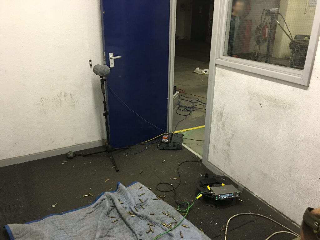 A sound effects library scene on Sonniss: microphone, cables, and gear set up for firearm SFX recording in a blue-lit room.