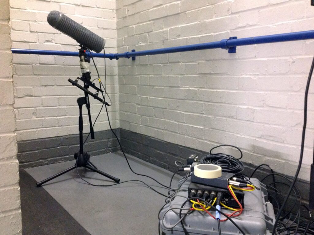 A professional microphone records new sounds for a sound effects library in a room with audio gear and white brick walls on Sonniss.