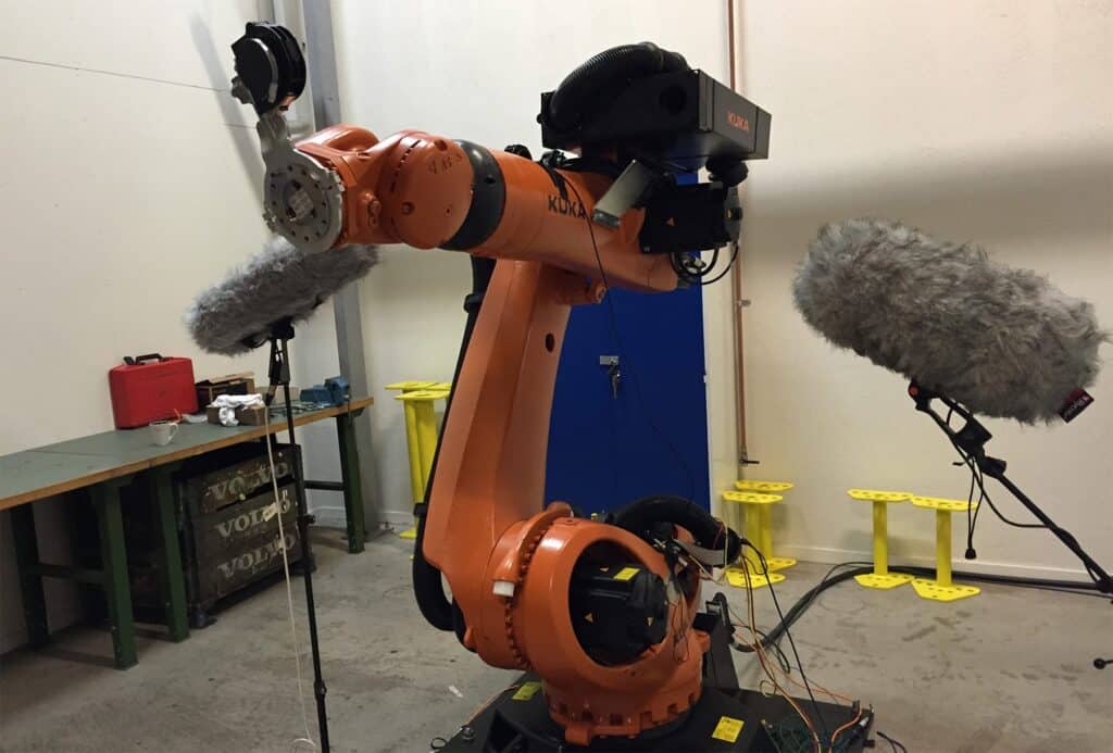 An orange robotic arm records unique sounds for an industrial sfx library in a workshop—perfect for hydraulic sound effects needs.