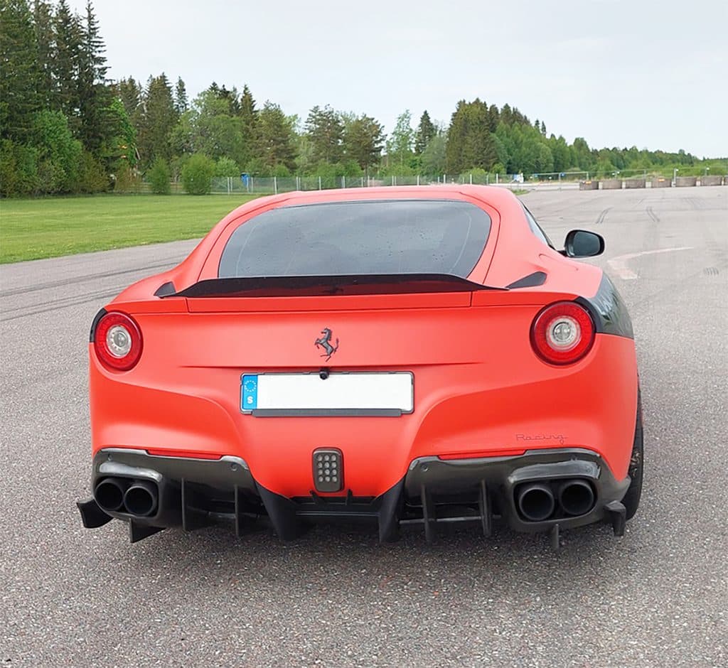 Rear view of a red Ferrari sports car on a road with green trees in the background. Perfect for your sfx library at Sonniss!