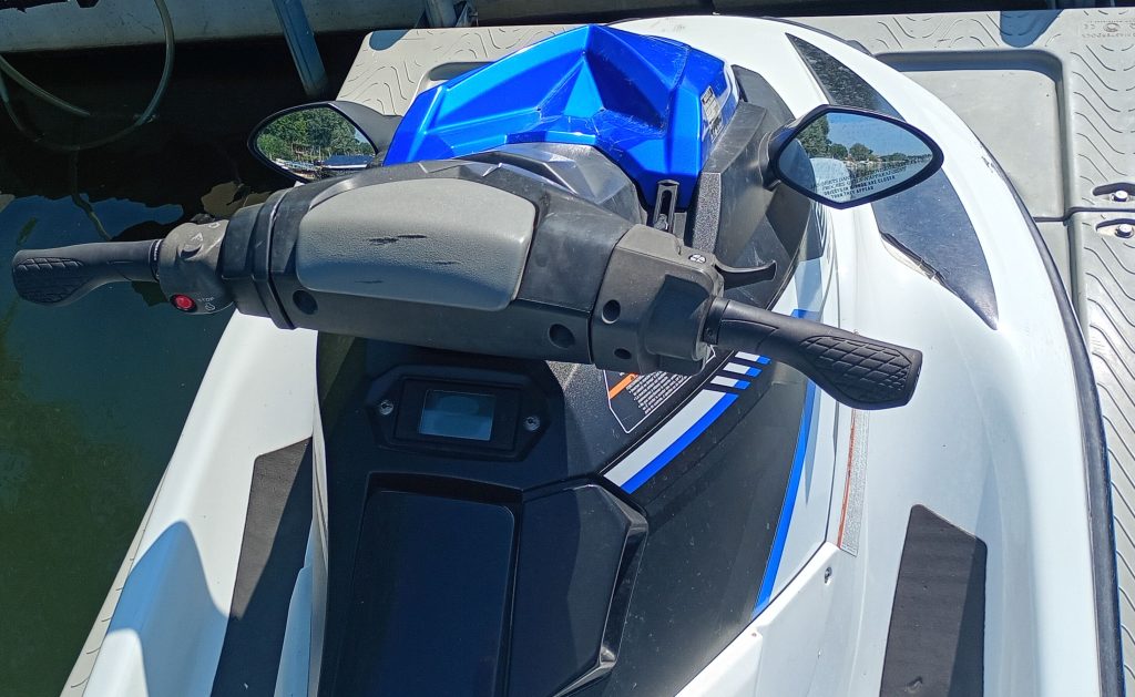 Close-up of a white and blue jet ski on a dock, highlighting the handlebars, mirrors, and digital display panel in bright sunlight.