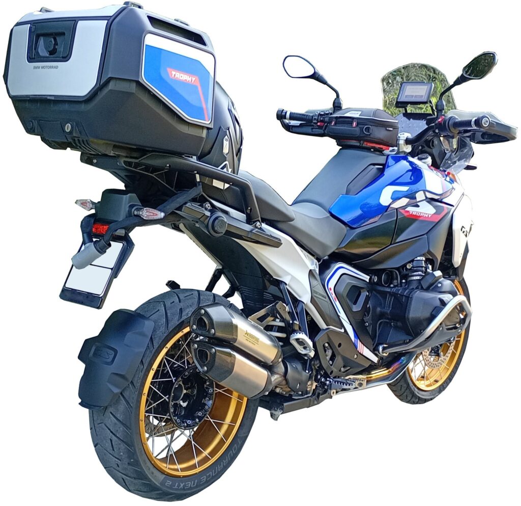 Blue and black adventure motorcycle featuring gold wheels, side and rear storage boxes, dual exhausts, and a digital display, viewed from the rear left angle against a white background.