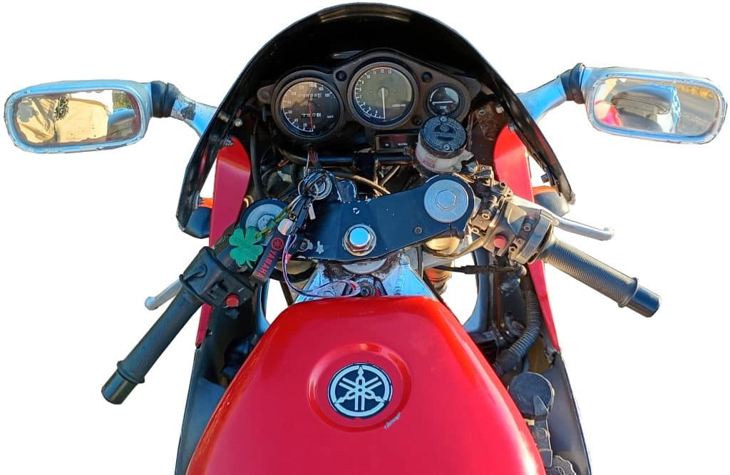 Yamaha motorcycle dashboard with visible handlebars, speedometer, mirrors, keys, and controls; red fuel tank in the foreground.