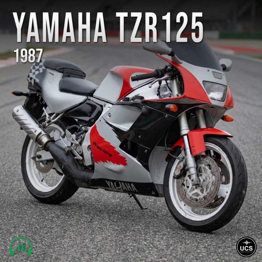 A 1987 Yamaha TZR125 motorcycle in red, black, and silver is parked on a racetrack. The bike has a sporty fairing and “Racing” lettering on the side.