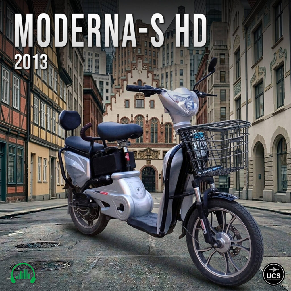 Silver 2013 Moderna-S HD electric scooter motorcycle with basket and backrest parked on a historic cobblestone street.